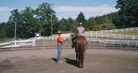 Young instructor teaching female student on horseback in riding pen Stock Footage 98304981