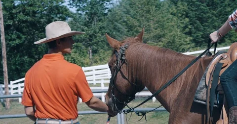 Young instructor teaching female student on horseback in riding pen Stock Footage 98314140