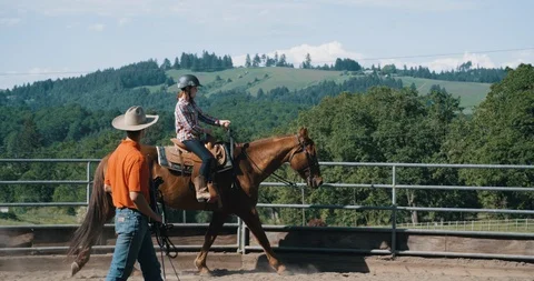Young instructor teaching female student on horseback in riding pen Stock Footage 105001041