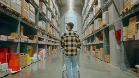 A young Interior designer man pushing supermarket cart looking for home decor Stock Footage 190089010