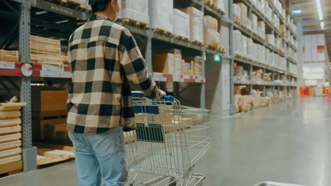 A young Interior designer man pushing supermarket cart looking for home decor Video stock 190100853