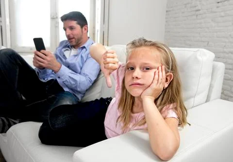 Young internet addict father using mobile phone ignoring his little sad daughter Stock Photos
