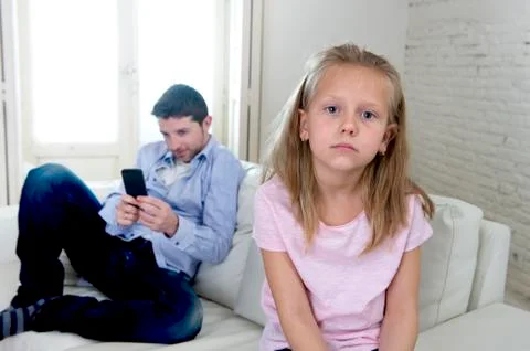Young internet addict father using mobile phone ignoring his little sad daughter Stock Photos