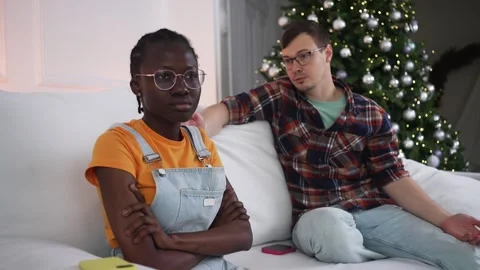 Young interracial couple argue on sofa during holidays; woman sits silent and Stock Footage 344988266