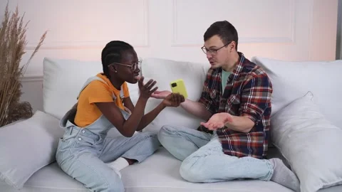 Young interracial couple engaged in a heated disagreement over the phone, as Stock Footage 344988147