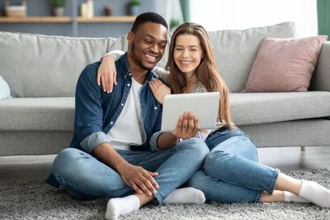 Young Interracial Spouses Using Digital Tablet Together While Resting At Home Stock Photos