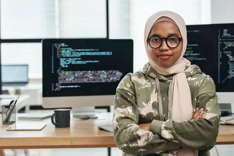 Young IT engineer in hijab sitting against computer screens with coded data 스톡 사진