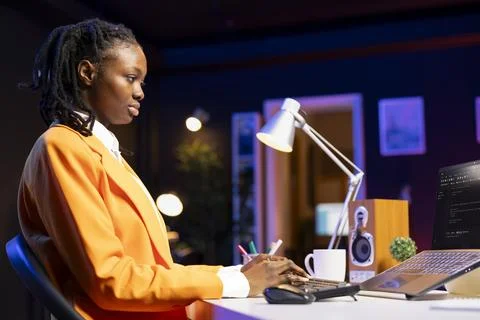 Young IT expert fixing database errors while working from dimly lit living room Photos