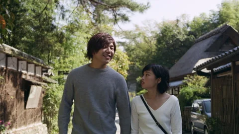 Young Japanese couple on a date talking and walking past houses down a sidewalk Stock Footage 199455287
