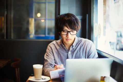 Young Japanese man enjoying a day out in London, sitting in a cafe, using laptop Stock Photos