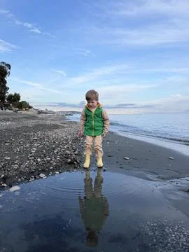 Young kid exploring shoreline with waves gently approaching feet. Reflection in Stock Photos