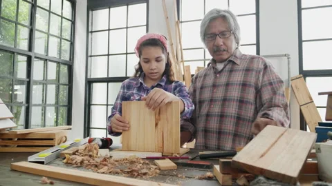 Young kid girl learn to work carpentry with grandfather in wooden shed at home.  Stock Footage 153477429