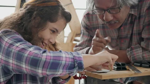 Young kid girl learn to work carpentry with grandfather in wooden shed at home.  Stock Footage 153477544