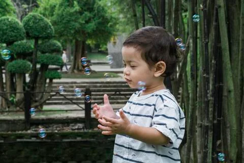 Young kid playing with bubble under bright sunny day at public park Foto stock