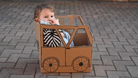 Young kid playing inside a cardboard made car wearing surgical mask Stock Footage 128930689