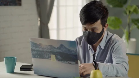 Young Korean man with face mask working on laptop at home Stock Footage
