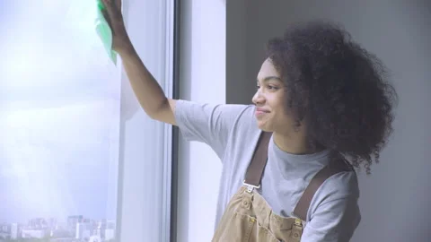 A young lady is cleaning the window in a well-lit room in 4K. Stock Footage 313350298