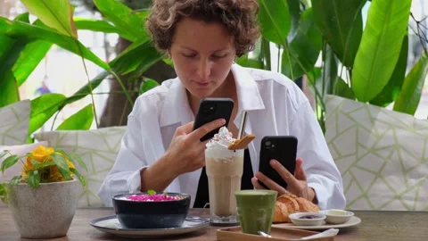Young lady comparing two phones by taking snaps of large latte with cream and Stock Footage 166455743
