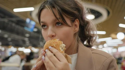 Young lady devouring crispy burger happily at mall, lively scene of young woman Video stock 326128383