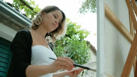 Young lady drawing on white canvas standing outdoors. Stock Footage 76593377