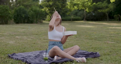 Young lady dressed in white T-shirt and blue aprons, sitting on the grass Stock Footage 200021656