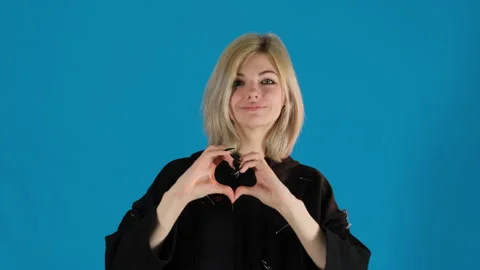 Young lady forms heart shape with hands on blue background Stock Footage 306504785