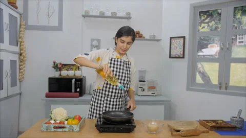 A young lady inside her modern kitchen pours some oil in the pan before cooking Video stock 155878584