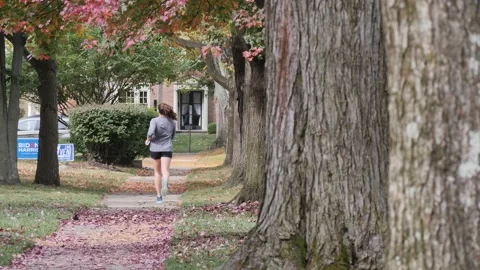 YOUNG LADY JOGGING IN FALL, OLD NEIGHBORHOOD, REAR VIEW, SLO-MO Stock Footage 143019077