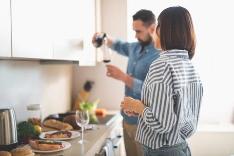 Young lady looking at boyfriend while he pouring wine into glass Stock Photos