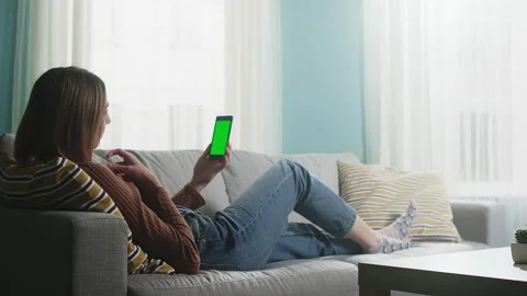 Young lady is lying on a beige sofa and talking on a video call. Chromakey Video stock 146754167