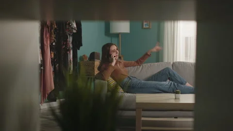 Young lady is lying on couch and anxiously talking on phone Stock Footage 139864524
