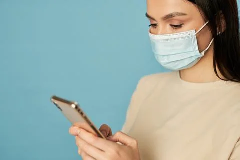 Young lady in mask using smartphone and looking at screen in studio Stock Photos