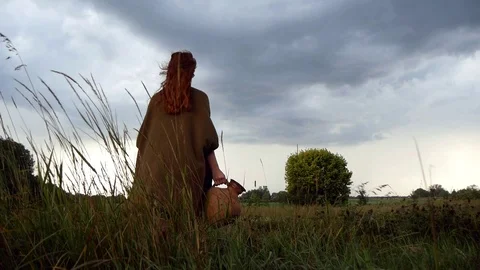 Young Lady In Poncho Standing In Grass With Clay Pitcher In Hand In Windy Day Stock Footage 127540722