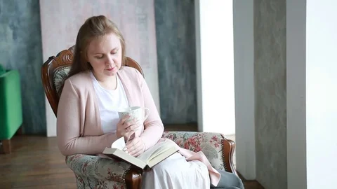 Young lady read book and drink coffee at the sofa near the window Stock Footage 75473170