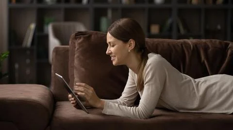 Young lady rest on couch scroll news on tablet online Stock Photos