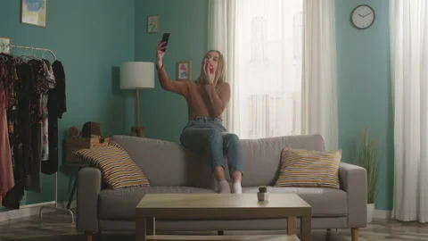 Young lady sits on the back of the sofa and takes a selfie Stock Footage 149144366