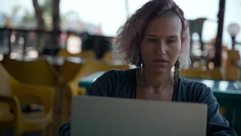 A young lady sits at a computer in a cafe and diligently does her job. Stock Footage 234020367