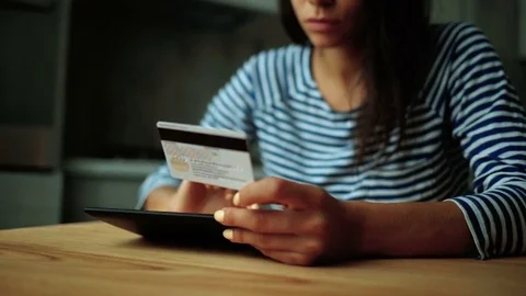 Young lady sitting on the kitchen with credit card and doing shopping online Stock Footage 73815029