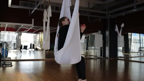Young lady is sitting on white hammock in fly yoga studio. Video stock 86469367