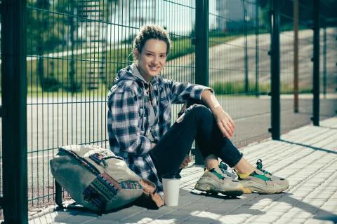 Young lady smiling while sitting on the ground by the chain link fence Stock Photos