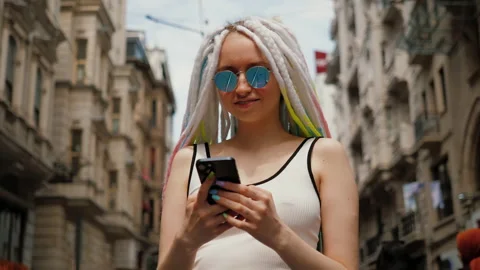 Young lady with sunglasses and dreadlocks using mobile phone outside in street Stock Footage 217437322