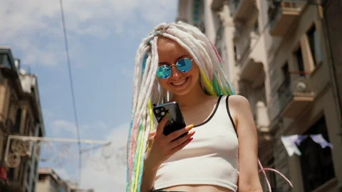 Young lady with sunglasses and dreadlocks using mobile phone outside in street Stock Footage 218374039