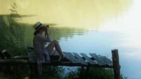 Young lady taking a pictures while sitting on a small dock on a beautiful lake. Stock Footage 156901956