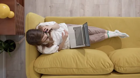 Young lady is talking phone while reclining on couch, From birds-eye perspective Video stock 249285574