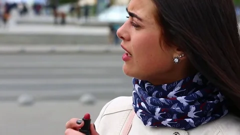 Young lady while looking on the mirror make her lips red lipstick on the street. Stock Footage 75582428