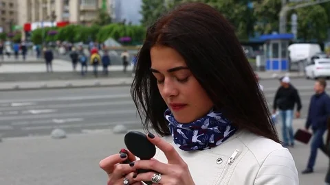 Young lady while looking on the mirror make her lips red lipstick on the street. Stock Footage 75582445