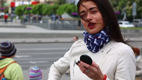 Young lady while looking on the mirror make her lips red lipstick on the street. Stock Footage 75582455