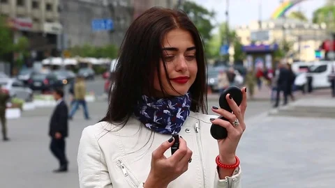 Young lady while looking on the mirror make her lips red lipstick on the street. Stock Footage 75582476