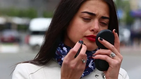 Young lady while looking on the mirror make her lips red lipstick on the street. Stock Footage 75582503