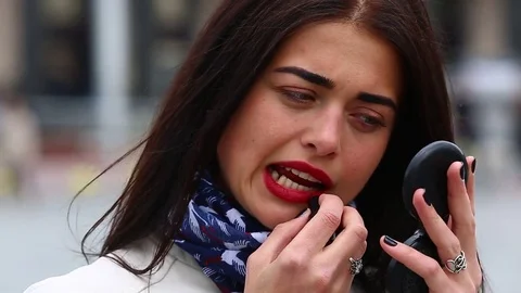 Young lady while looking on the mirror make her lips red lipstick on the street. Stock Footage 75582543